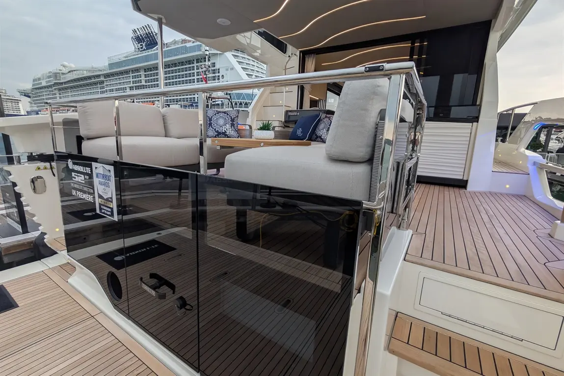 Luxury yacht deck featuring modern seating, glossy black panels, wooden flooring, and a backdrop of a large cruise ship.